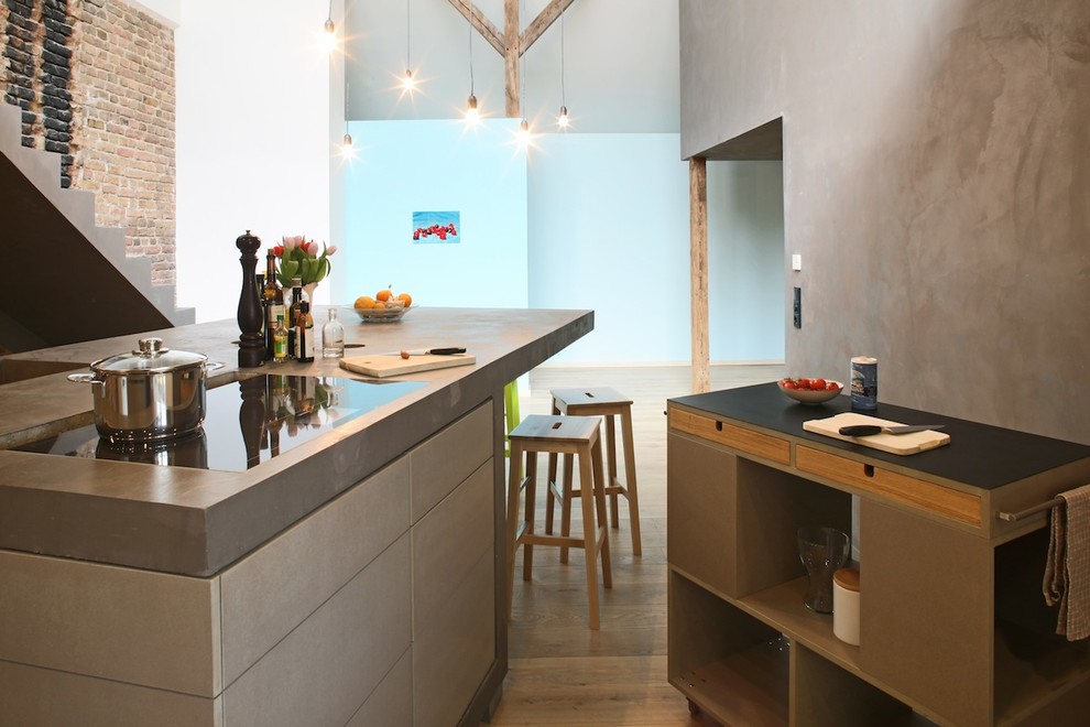Industrial open plan kitchen in Berlin with multiple islands, flat-panel cabinets, grey cabinets, concrete benchtops and medium hardwood floors.