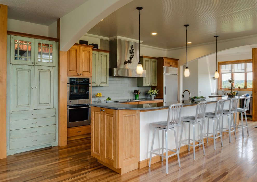 Traditional galley kitchen in Grand Rapids with raised-panel cabinets, green cabinets, grey splashback, subway tile splashback, stainless steel appliances, medium hardwood floors and with island.