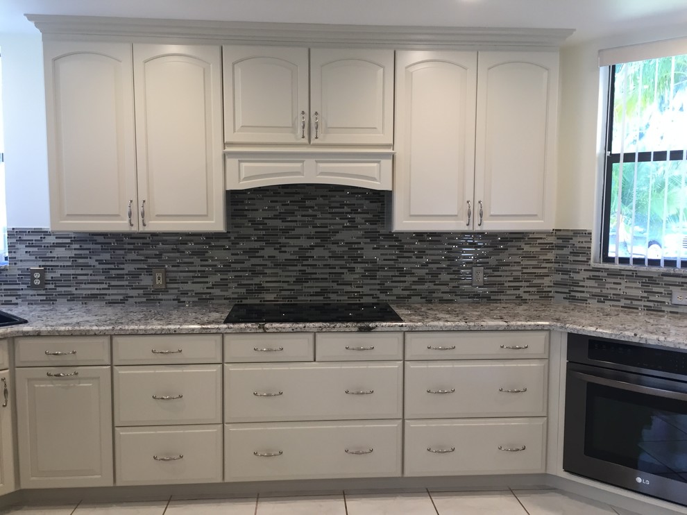 Photo of a medium sized traditional l-shaped kitchen/diner in Miami with a built-in sink, raised-panel cabinets, beige cabinets, granite worktops, glass sheet splashback, black appliances, porcelain flooring, an island, multi-coloured splashback, beige floors and beige worktops.