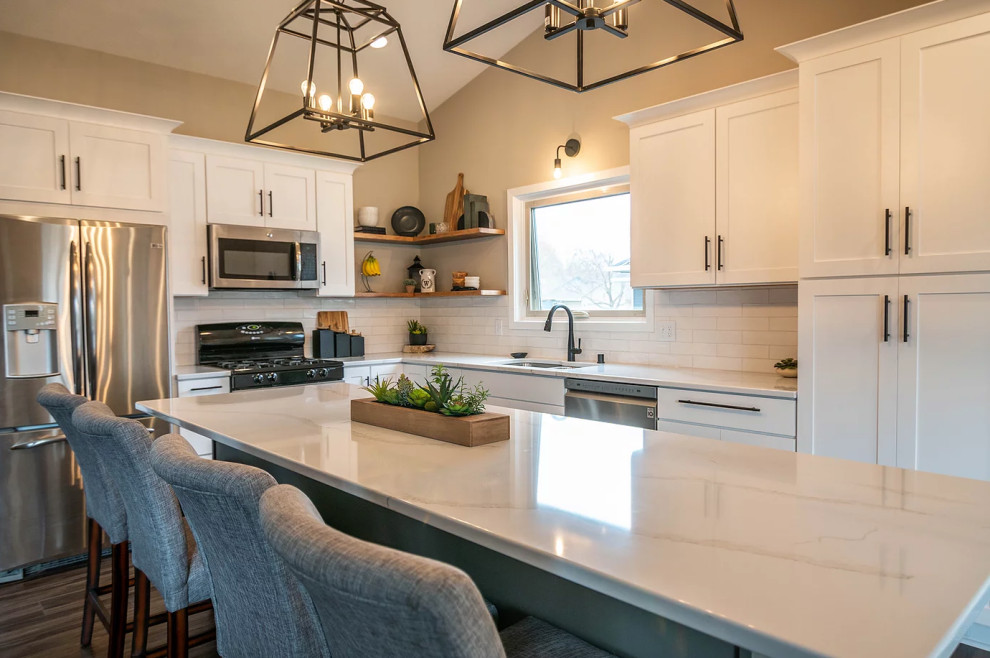 This is an example of a large transitional l-shaped eat-in kitchen in Minneapolis with an undermount sink, shaker cabinets, white cabinets, quartz benchtops, white splashback, ceramic splashback, stainless steel appliances, vinyl floors, with island, brown floor and white benchtop.