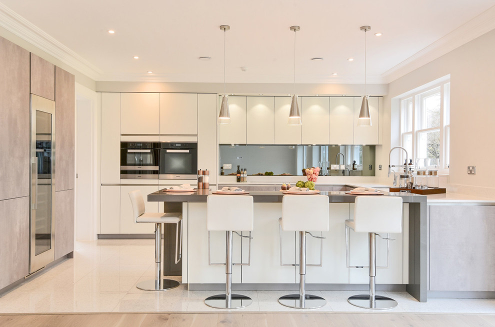 Mid-sized contemporary u-shaped eat-in kitchen in Berkshire with flat-panel cabinets, white cabinets, quartzite benchtops, mirror splashback, a peninsula, metallic splashback, beige floor and grey benchtop.
