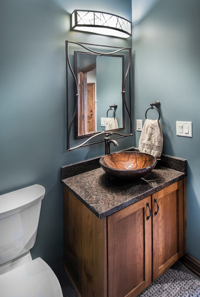 Inspiration for a mid-sized country powder room in Omaha with shaker cabinets, dark wood cabinets, granite benchtops, a two-piece toilet, blue walls, a vessel sink and brown benchtops.