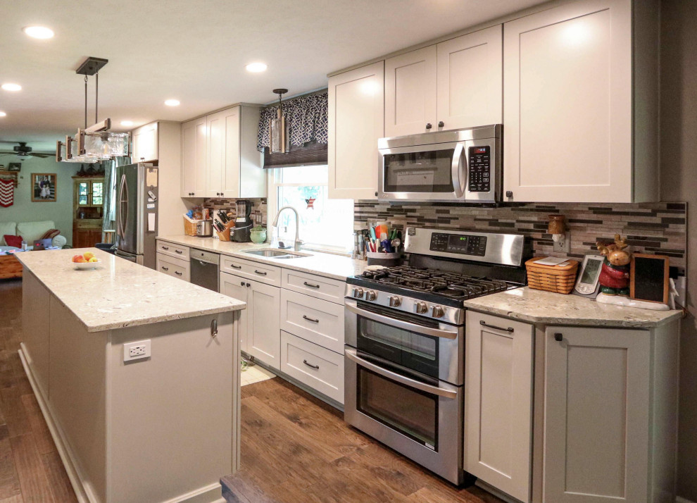 This is an example of a mid-sized transitional galley eat-in kitchen in Cleveland with an undermount sink, shaker cabinets, white cabinets, quartz benchtops, multi-coloured splashback, mosaic tile splashback, stainless steel appliances, medium hardwood floors, with island, brown floor and beige benchtop.