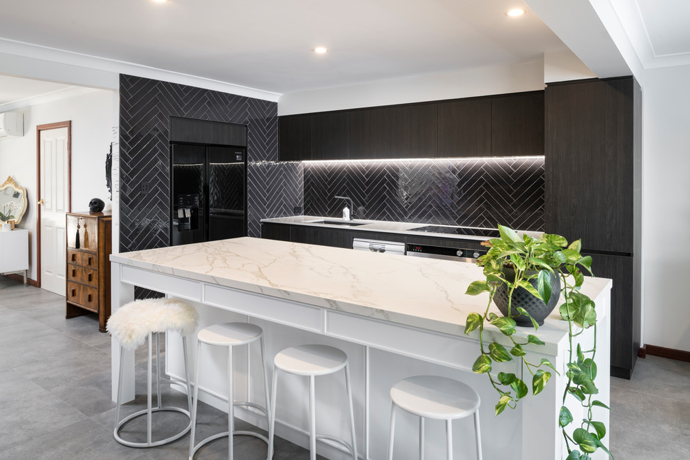 Photo of a mid-sized contemporary galley kitchen in Perth with an undermount sink, flat-panel cabinets, dark wood cabinets, black splashback, subway tile splashback, black appliances, cement tiles, with island, grey floor, white benchtop and marble benchtops.