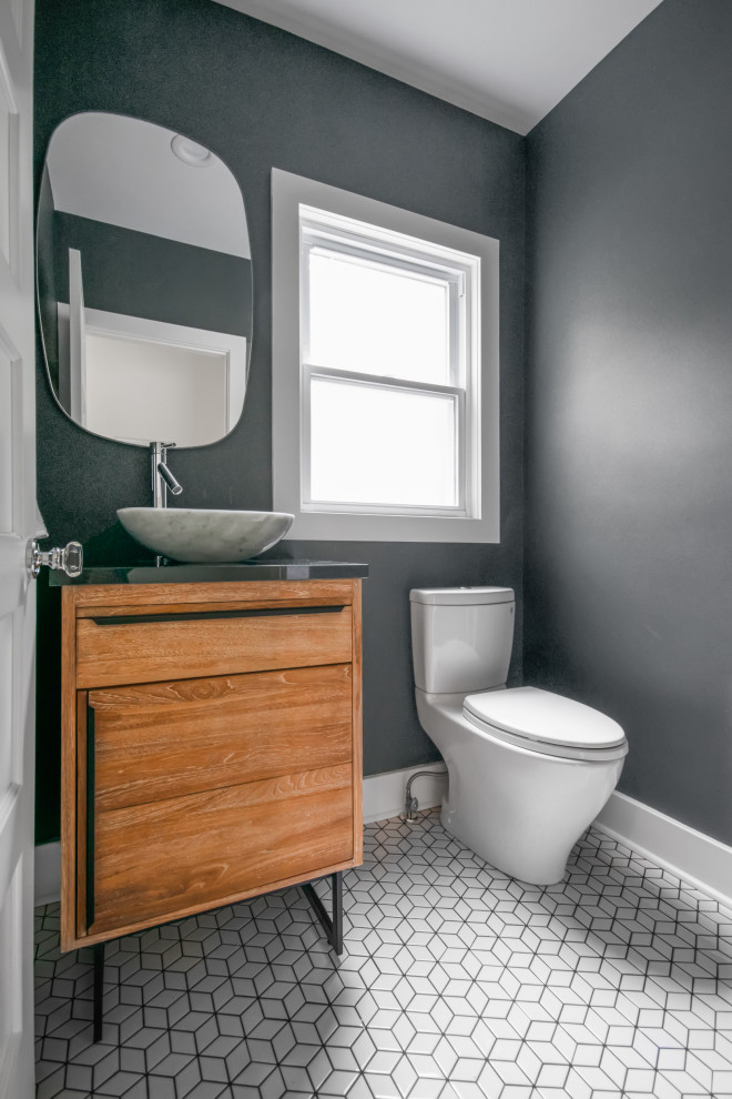 This is an example of a small modern powder room in New York with furniture-like cabinets, medium wood cabinets, a two-piece toilet, gray tile, grey walls, ceramic floors, a vessel sink, solid surface benchtops, white floor and grey benchtops.