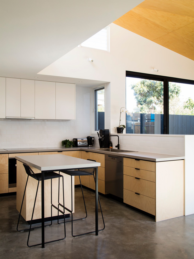 Contemporary l-shaped open plan kitchen in Melbourne with a drop-in sink, flat-panel cabinets, light wood cabinets, white splashback, stainless steel appliances, concrete floors, with island and grey floor.