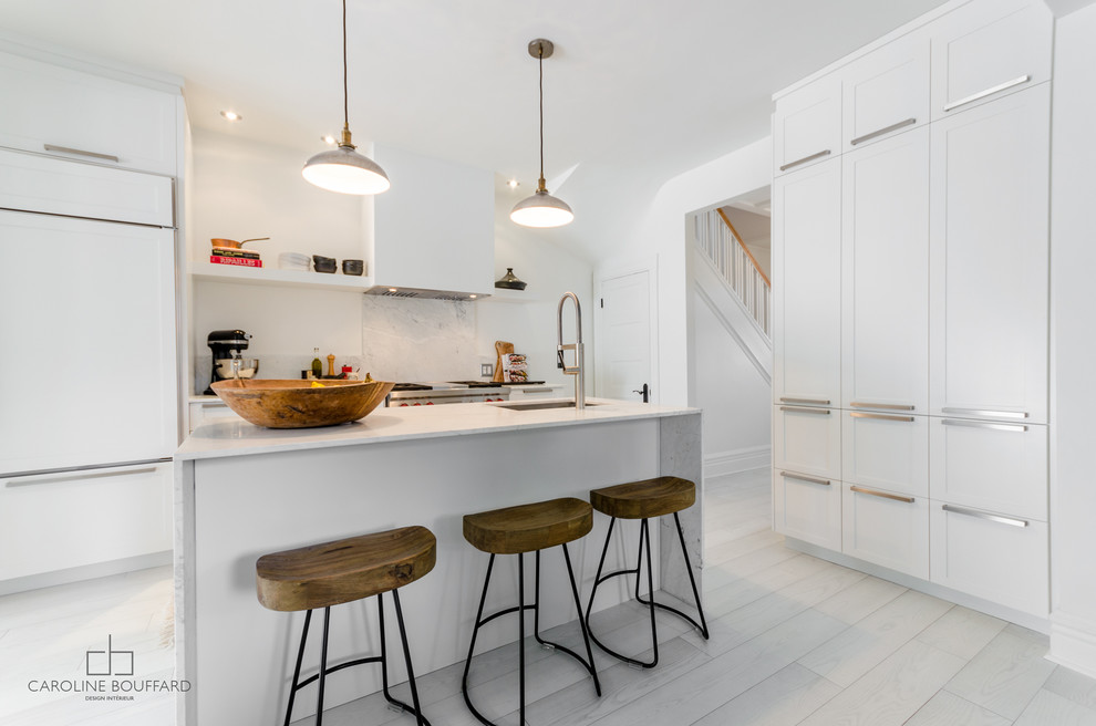 Transitional kitchen in Montreal with an undermount sink, shaker cabinets, white cabinets, marble benchtops, white splashback, stainless steel appliances, light hardwood floors and with island.