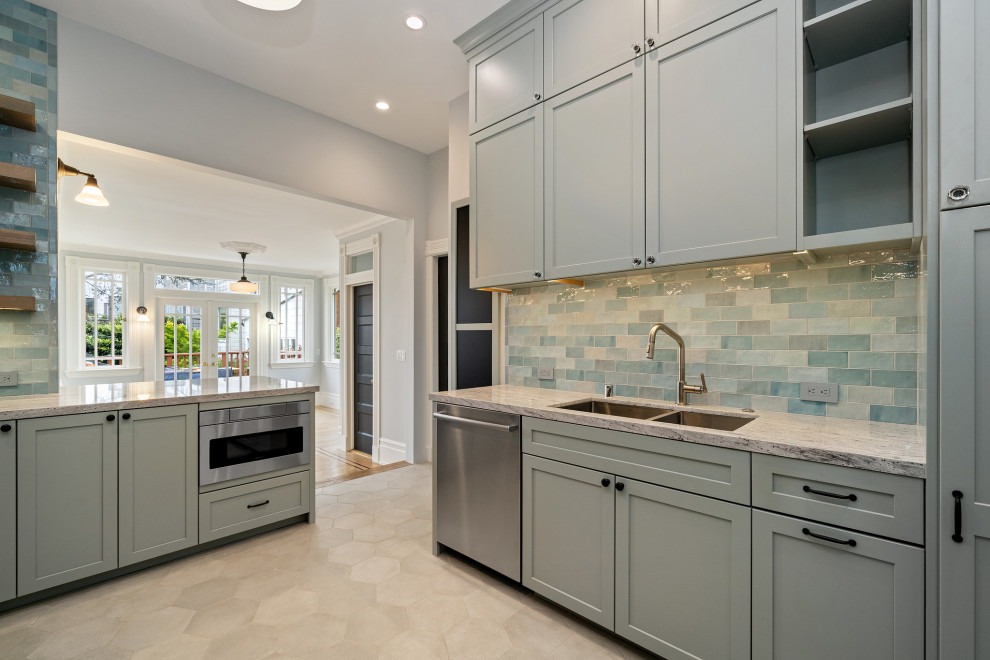 Idéer för ett stort klassiskt grå kök, med en dubbel diskho, luckor med infälld panel, grå skåp, granitbänkskiva, grönt stänkskydd, stänkskydd i glaskakel, rostfria vitvaror, klinkergolv i keramik, en köksö och beiget golv