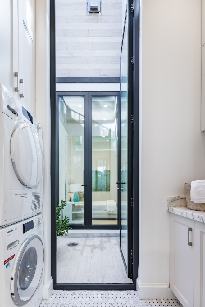 Small modern galley dedicated laundry room in San Francisco with a drop-in sink, shaker cabinets, white cabinets, marble benchtops, white walls, marble floors, a stacked washer and dryer, yellow floor and white benchtop.