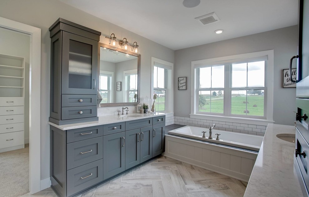 Design ideas for a small country master bathroom in Grand Rapids with shaker cabinets, turquoise cabinets, a drop-in tub, white tile, grey walls, medium hardwood floors, an undermount sink, solid surface benchtops, beige floor and a hinged shower door.
