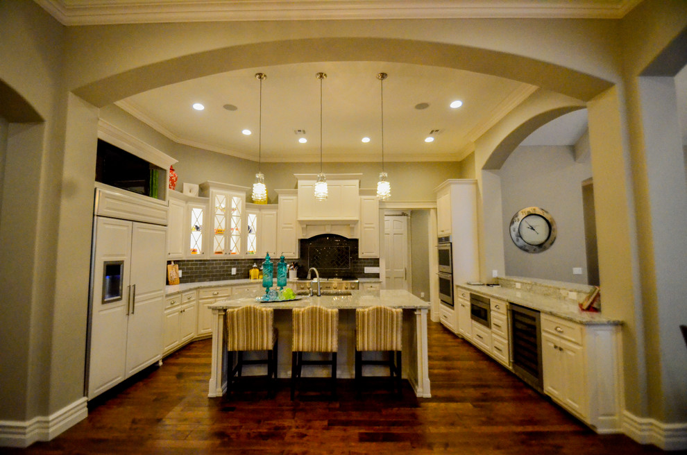 Open concept kitchen - large transitional u-shaped dark wood floor open concept kitchen idea with an island, a double-bowl sink, raised-panel cabinets, white cabinets, granite countertops, gray backsplash and stainless steel appliances