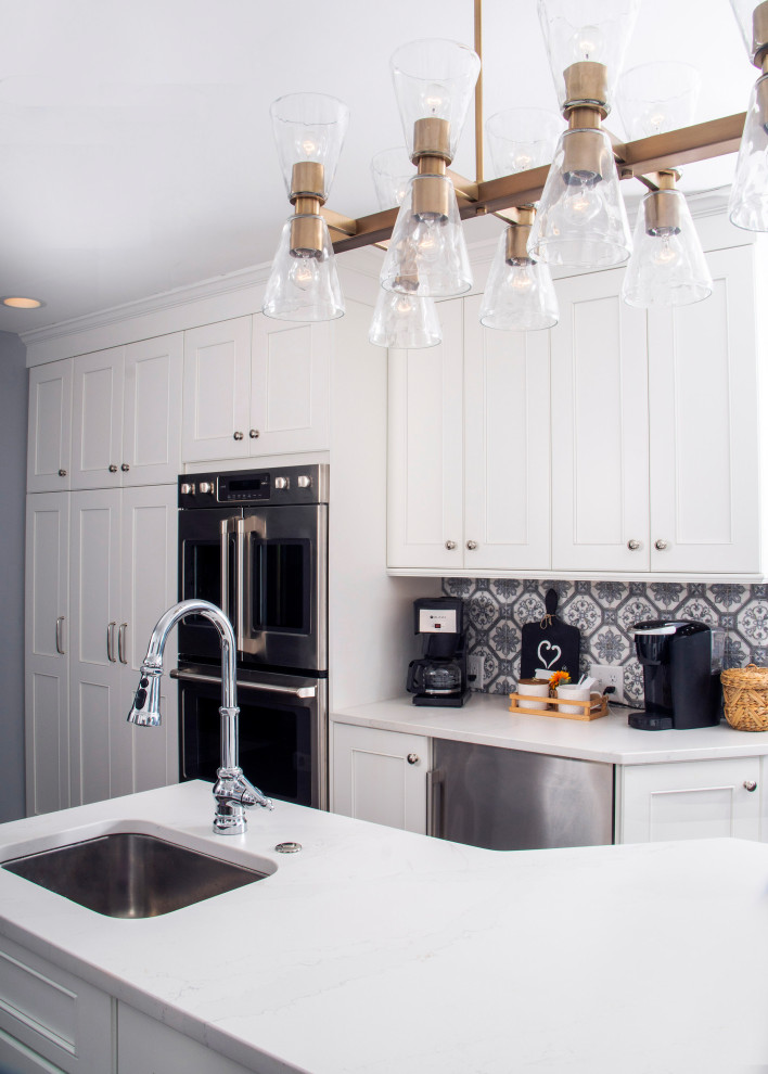 Example of a mid-sized transitional l-shaped medium tone wood floor and brown floor eat-in kitchen design in St Louis with a farmhouse sink, recessed-panel cabinets, white cabinets, quartz countertops, blue backsplash, ceramic backsplash, stainless steel appliances, an island and white countertops