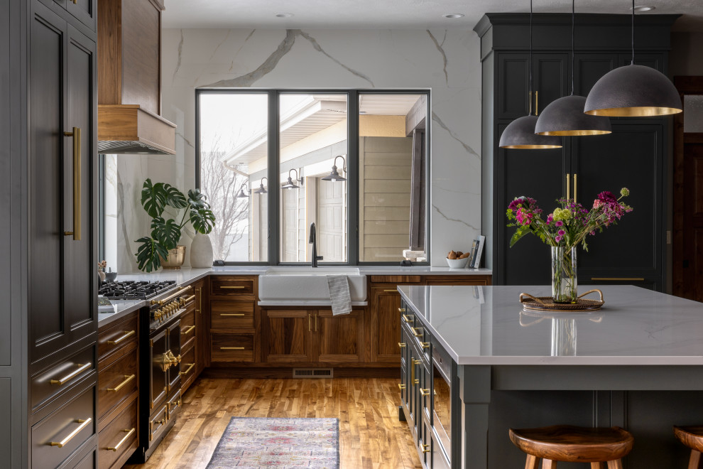 Example of a mid-sized transitional l-shaped brown floor and medium tone wood floor eat-in kitchen design with a farmhouse sink, quartz countertops, white backsplash, quartz backsplash, black appliances, an island, white countertops, recessed-panel cabinets and medium tone wood cabinets