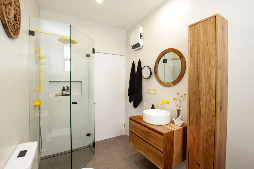 Photo of a mid-sized eclectic master bathroom in Sydney with medium wood cabinets, a freestanding tub, a corner shower, a two-piece toilet, white tile, white walls, a vessel sink, grey floor, a hinged shower door, a niche, a single vanity and a floating vanity.