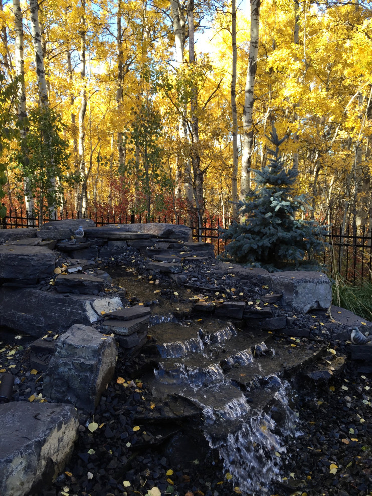 Design ideas for a large traditional backyard xeriscape in Calgary with with waterfall and river rock.