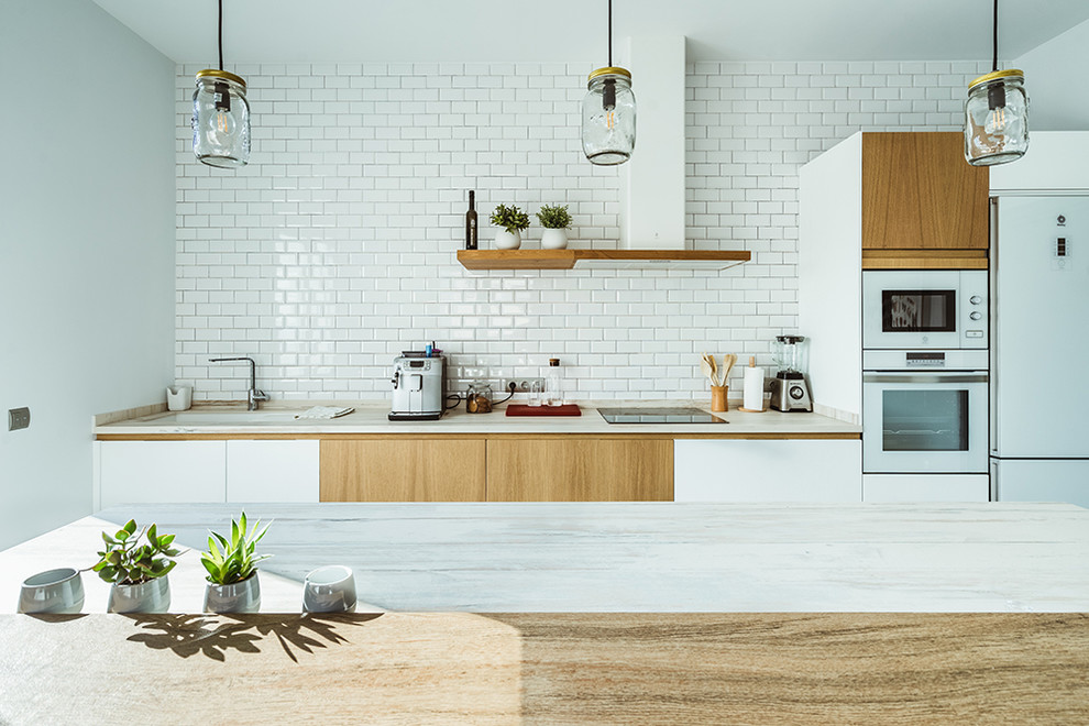 Design ideas for a scandinavian single-wall separate kitchen in Madrid with an integrated sink, flat-panel cabinets, medium wood cabinets, wood benchtops, white splashback, subway tile splashback, white appliances, light hardwood floors, with island, brown floor and beige benchtop.