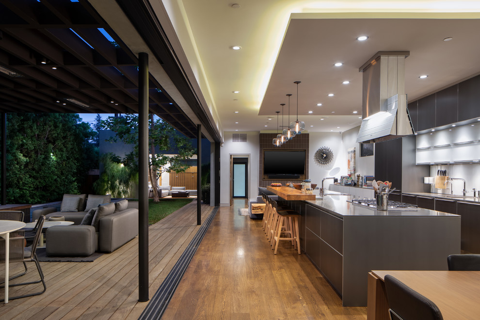 Photo of a contemporary l-shaped eat-in kitchen in Los Angeles with an undermount sink, flat-panel cabinets, grey cabinets, white splashback, medium hardwood floors, with island, brown floor and grey benchtop.