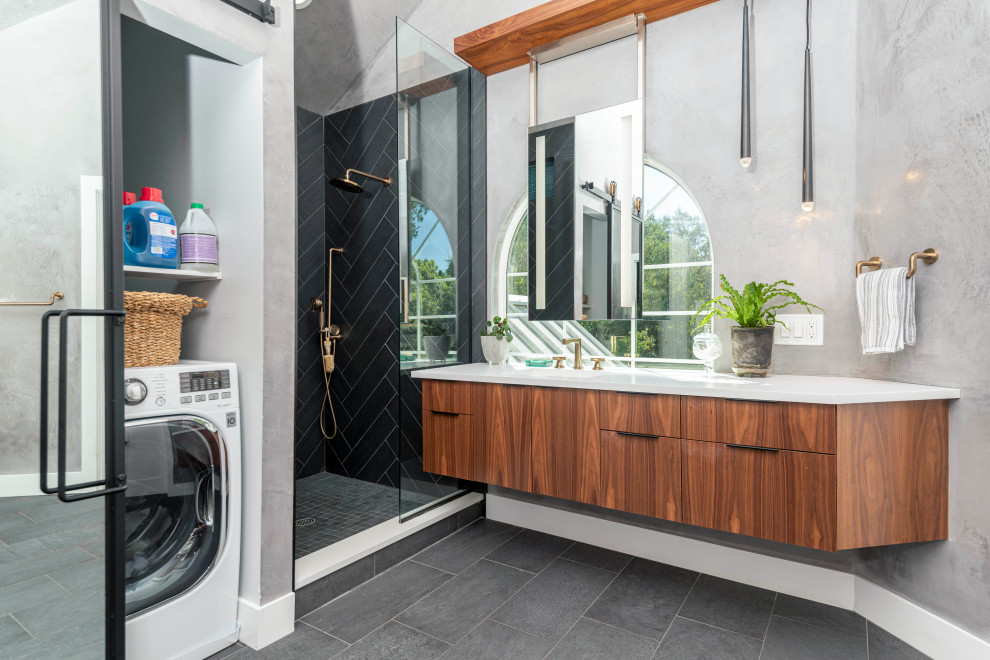This is an example of a contemporary bathroom in Orlando with flat-panel cabinets, medium wood cabinets, an alcove shower, grey walls, an undermount sink, grey floor, a hinged shower door, white benchtops, a laundry, a single vanity and a floating vanity.