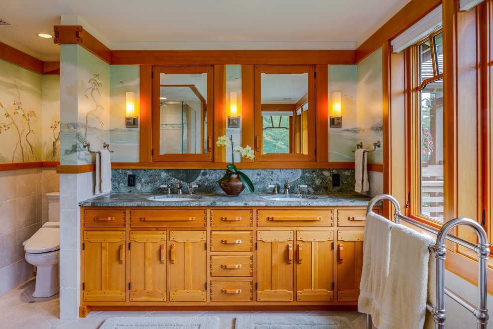 This is an example of a mid-sized arts and crafts master bathroom in Portland Maine with an undermount sink, furniture-like cabinets, medium wood cabinets, granite benchtops, a drop-in tub, a curbless shower, a two-piece toilet, beige tile, stone tile, multi-coloured walls, limestone floors and beige floor.