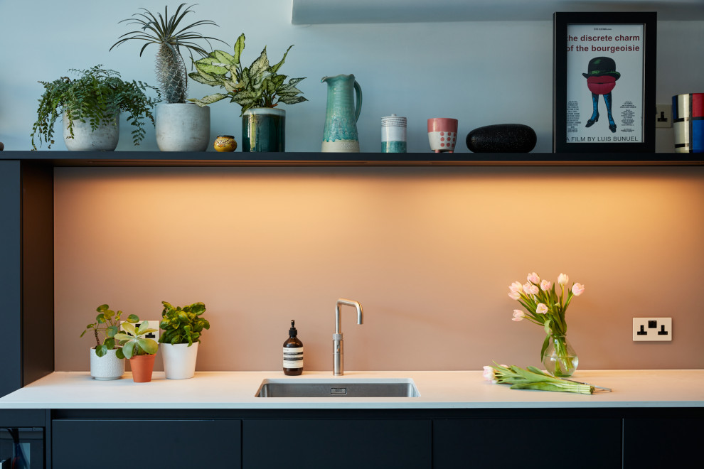 This is an example of a medium sized modern u-shaped kitchen/diner in London with an integrated sink, flat-panel cabinets, black cabinets, engineered stone countertops, pink splashback, glass sheet splashback, stainless steel appliances, an island and white worktops.