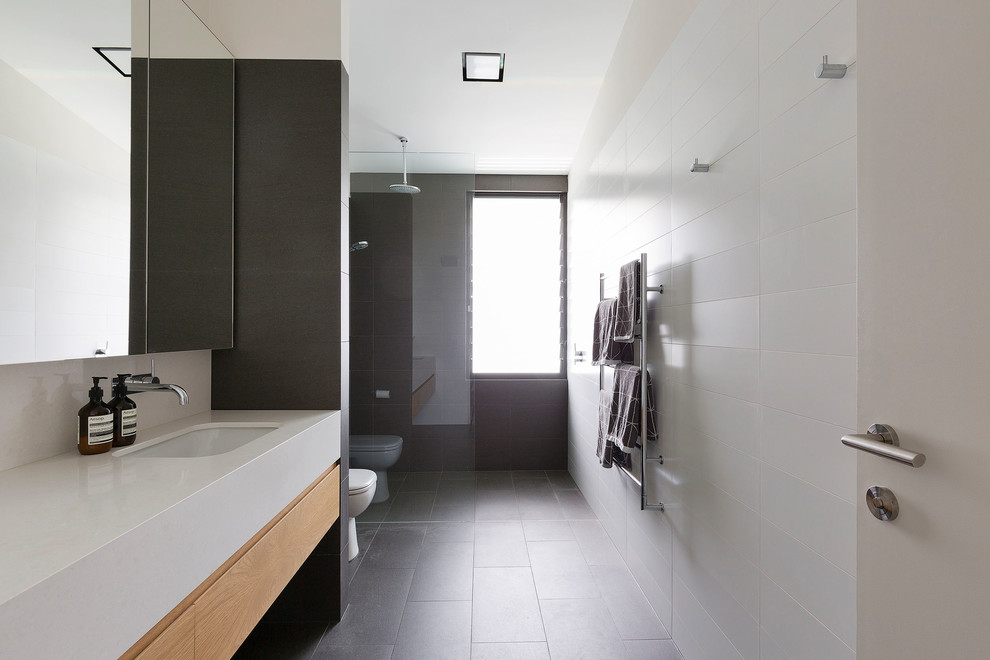 This is an example of a large contemporary master bathroom in Sydney with flat-panel cabinets, light wood cabinets, a curbless shower, a one-piece toilet, white tile, porcelain tile, white walls, ceramic floors, an undermount sink, engineered quartz benchtops, grey floor, an open shower and white benchtops.