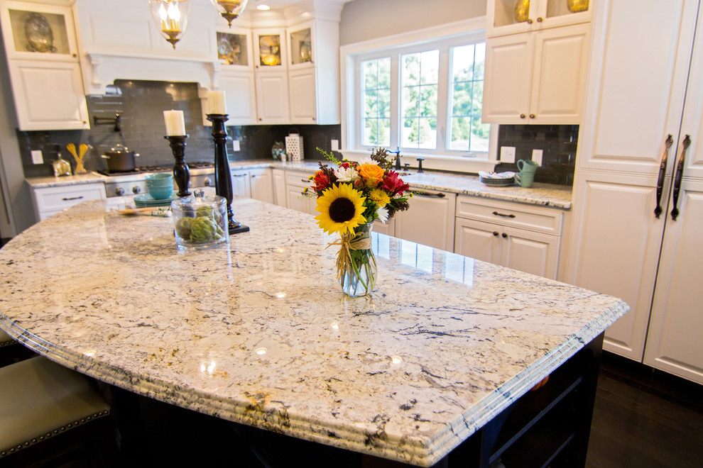 Example of a transitional l-shaped dark wood floor kitchen design in Providence with a farmhouse sink, raised-panel cabinets, granite countertops, gray backsplash, glass tile backsplash, paneled appliances and an island
