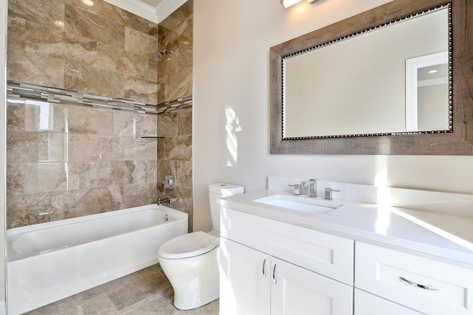 This is an example of a mid-sized transitional 3/4 bathroom in New Orleans with flat-panel cabinets, white cabinets, an alcove tub, an alcove shower, a one-piece toilet, beige tile, beige walls, an undermount sink, marble, travertine floors, engineered quartz benchtops and beige floor.