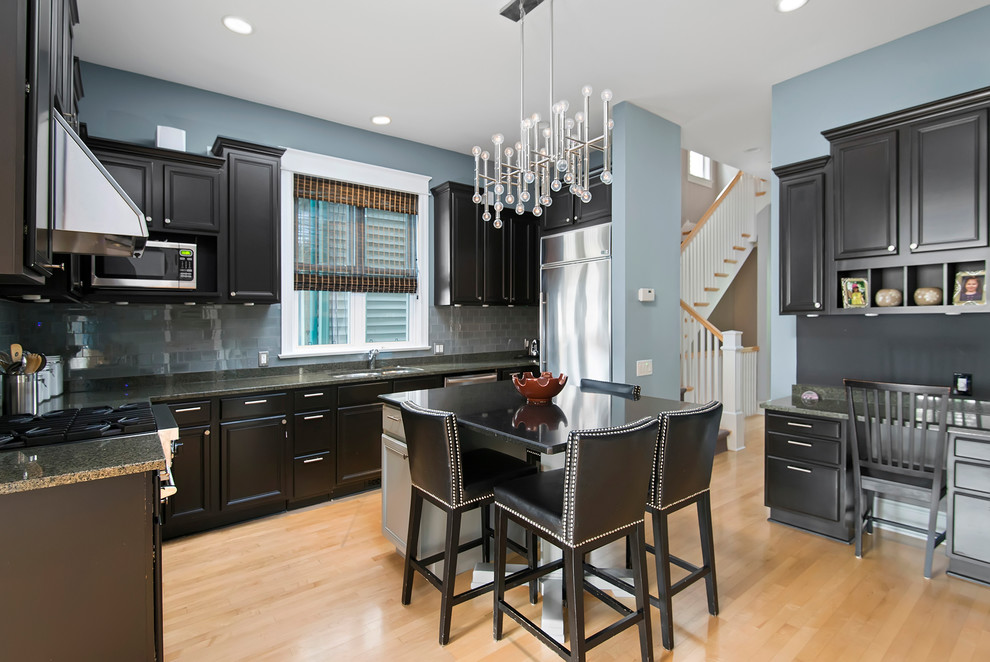 Inspiration for a transitional u-shaped kitchen in Chicago with a double-bowl sink, raised-panel cabinets, black cabinets, grey splashback, subway tile splashback, stainless steel appliances, medium hardwood floors and with island.