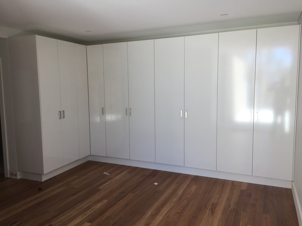 Cette photo montre une grande armoire encastrée tendance neutre avec placards, des portes de placard blanches, parquet en bambou et un sol marron.