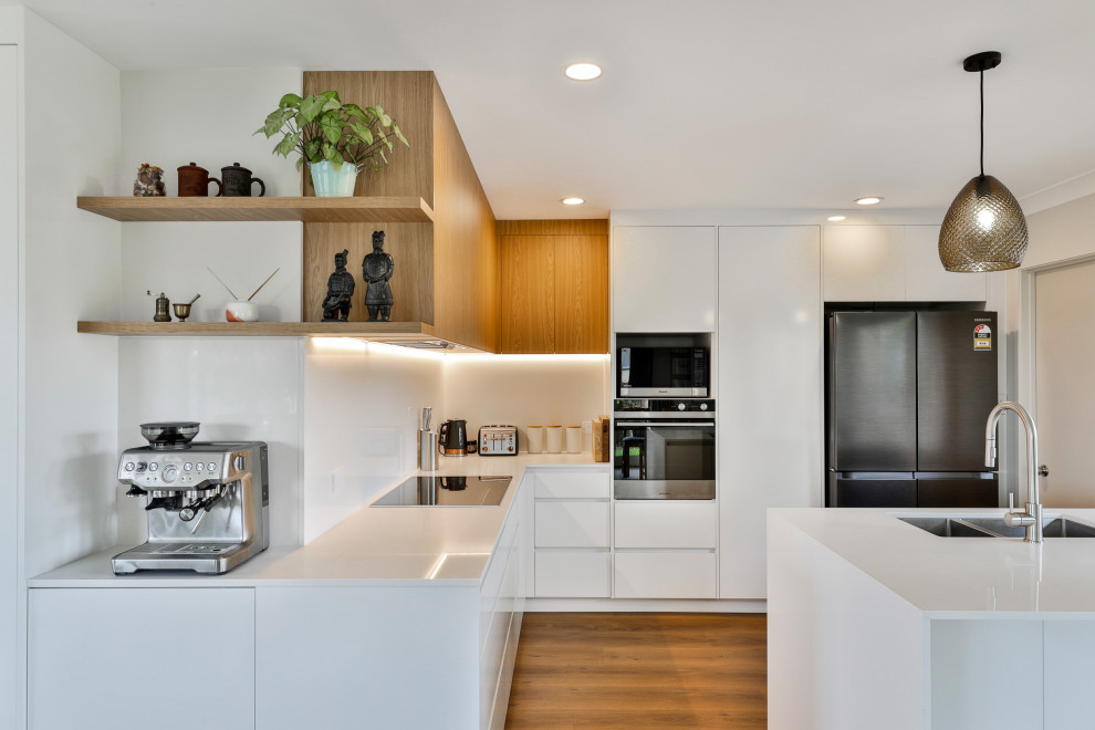 Design ideas for a mid-sized contemporary l-shaped eat-in kitchen in Auckland with a double-bowl sink, flat-panel cabinets, white cabinets, quartz benchtops, white splashback, engineered quartz splashback, stainless steel appliances, vinyl floors, a peninsula, brown floor and white benchtop.