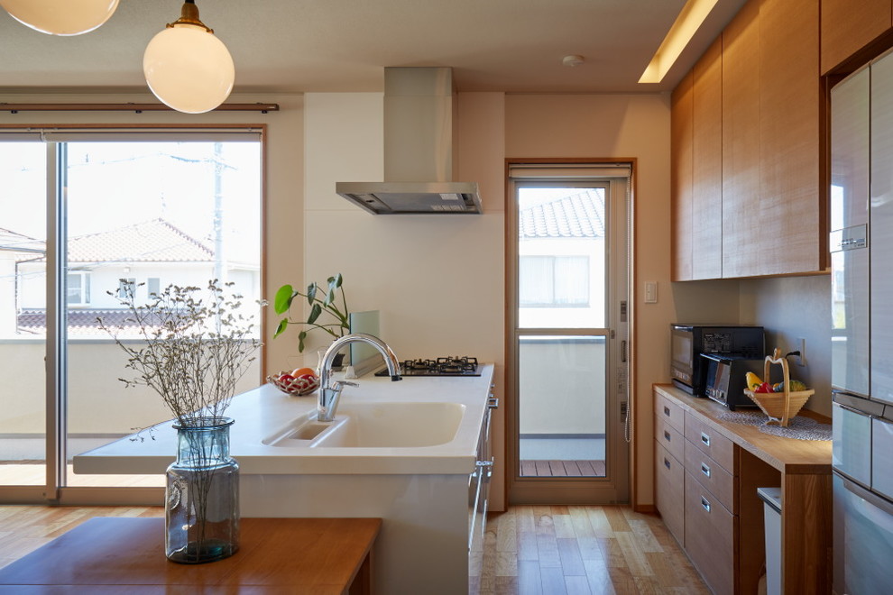 Photo of an asian galley kitchen in Other with an integrated sink, flat-panel cabinets, medium wood cabinets, glass sheet splashback, stainless steel appliances, light hardwood floors and a peninsula.