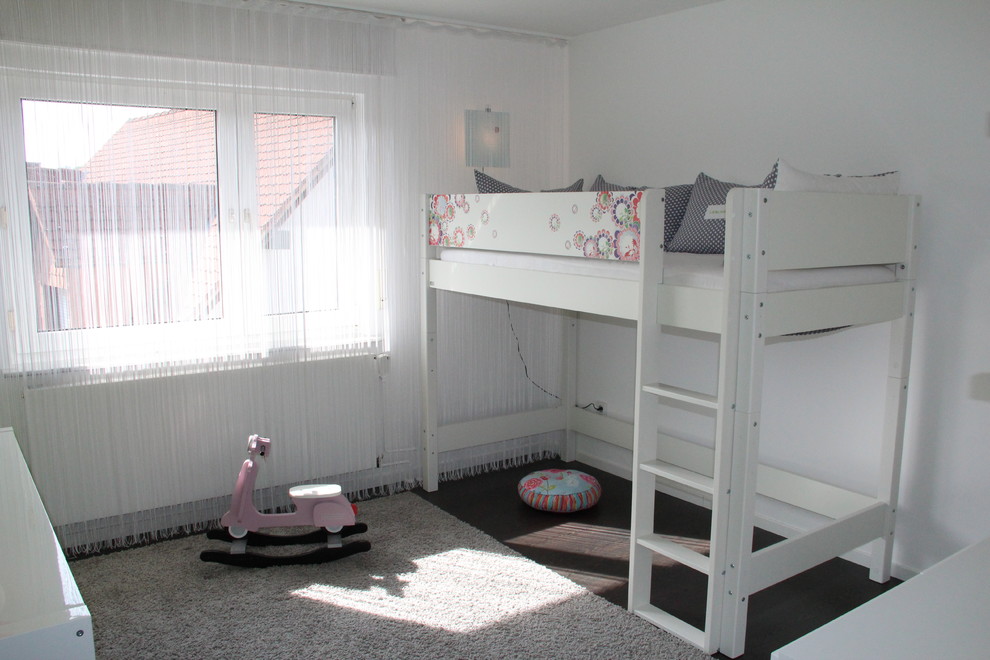 This is an example of a mid-sized contemporary kids' bedroom for kids 4-10 years old and girls in Bonn with white walls and dark hardwood floors.
