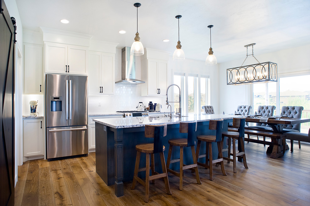 Inspiration for a mid-sized transitional l-shaped medium tone wood floor and brown floor eat-in kitchen remodel with a farmhouse sink, raised-panel cabinets, white cabinets, granite countertops, white backsplash, subway tile backsplash, stainless steel appliances and an island