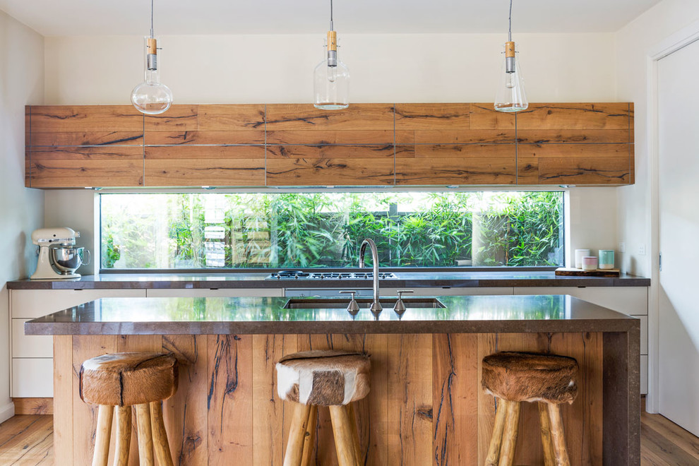 Inspiration for a country galley open plan kitchen in Melbourne with an undermount sink, flat-panel cabinets, medium wood cabinets, glass sheet splashback, medium hardwood floors, with island and brown floor.
