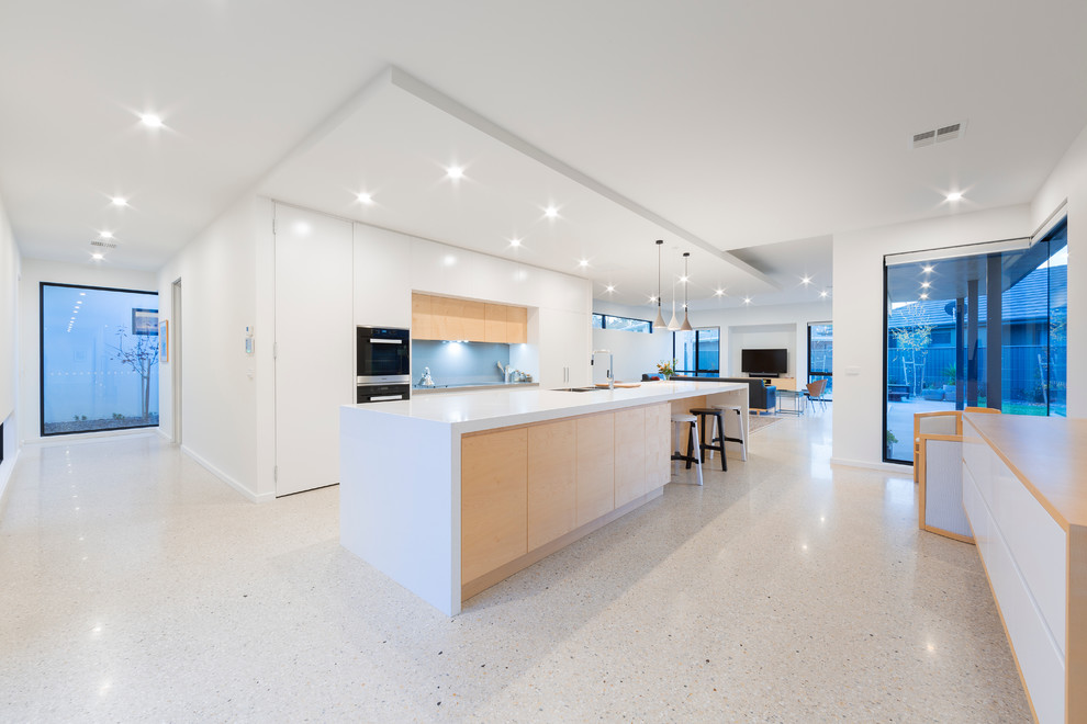 Photo of a large contemporary galley kitchen pantry in Canberra - Queanbeyan with an undermount sink, flat-panel cabinets, white cabinets, solid surface benchtops, blue splashback, glass sheet splashback, stainless steel appliances, terrazzo floors and with island.