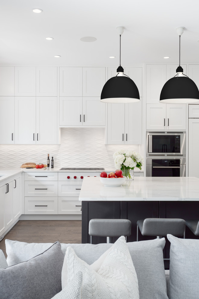Design ideas for a large transitional l-shaped kitchen in Vancouver with a double-bowl sink, recessed-panel cabinets, white cabinets, quartz benchtops, white splashback, porcelain splashback, stainless steel appliances, medium hardwood floors, with island, brown floor and white benchtop.