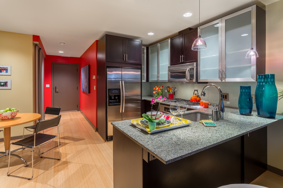 Photo of a small contemporary u-shaped eat-in kitchen in Seattle with an undermount sink, glass-front cabinets, black cabinets, granite benchtops, green splashback, glass sheet splashback, stainless steel appliances, bamboo floors, a peninsula and yellow floor.