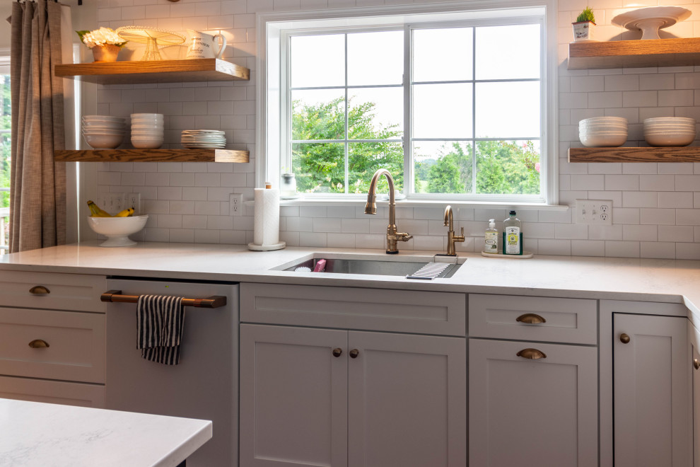 Mid-sized transitional l-shaped medium tone wood floor and brown floor open concept kitchen photo with an undermount sink, shaker cabinets, white cabinets, quartzite countertops, white backsplash, ceramic backsplash, white appliances, an island and white countertops