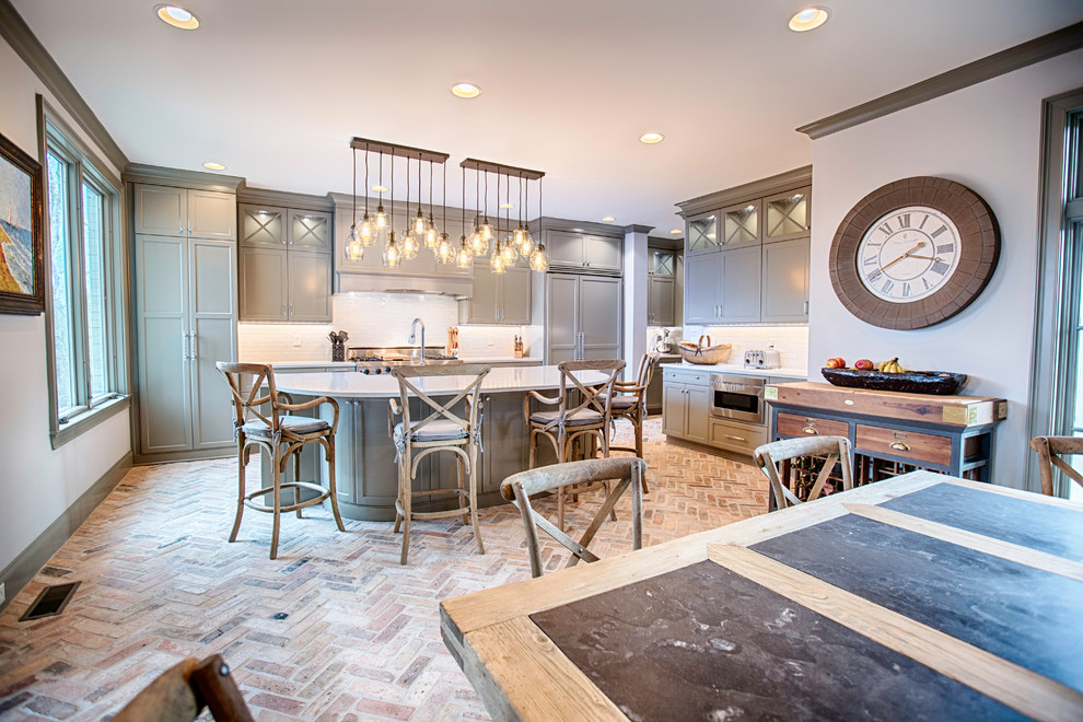 Eat-in kitchen - large transitional l-shaped brick floor and multicolored floor eat-in kitchen idea in Birmingham with a farmhouse sink, flat-panel cabinets, gray cabinets, quartzite countertops, gray backsplash, subway tile backsplash, stainless steel appliances and an island