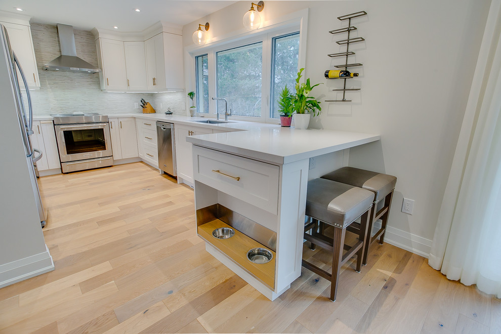 Design ideas for an expansive transitional eat-in kitchen in Toronto with an undermount sink, shaker cabinets, white cabinets, quartz benchtops, multi-coloured splashback, porcelain splashback, stainless steel appliances, medium hardwood floors, a peninsula and white benchtop.