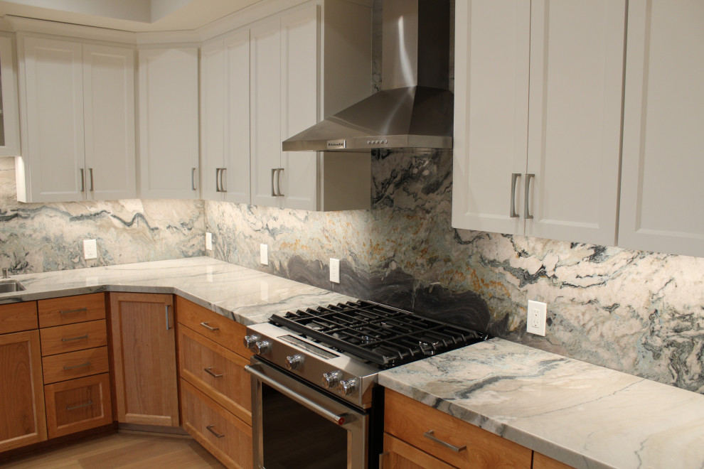 Large transitional l-shaped medium tone wood floor, brown floor and vaulted ceiling kitchen photo in San Francisco with an undermount sink, shaker cabinets, medium tone wood cabinets, granite countertops, multicolored backsplash, stone slab backsplash, stainless steel appliances, an island and multicolored countertops