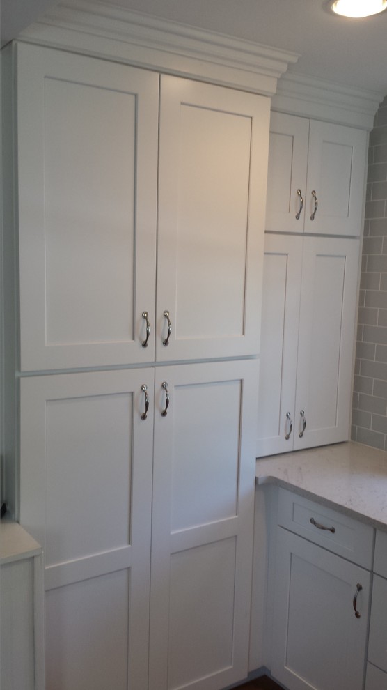 Example of a small transitional u-shaped light wood floor enclosed kitchen design in New York with an undermount sink, shaker cabinets, white cabinets, solid surface countertops, gray backsplash, subway tile backsplash, stainless steel appliances and an island