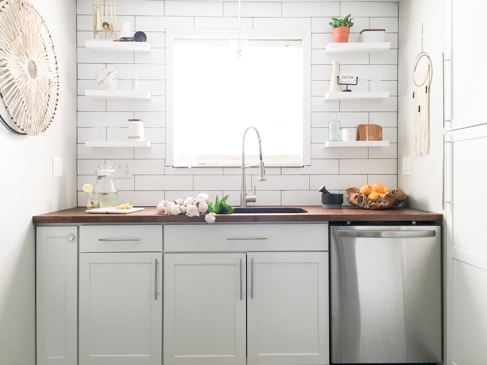 Inspiration for a small country u-shaped separate kitchen in Indianapolis with a drop-in sink, shaker cabinets, white cabinets, wood benchtops, white splashback, subway tile splashback, stainless steel appliances, ceramic floors, black floor and brown benchtop.