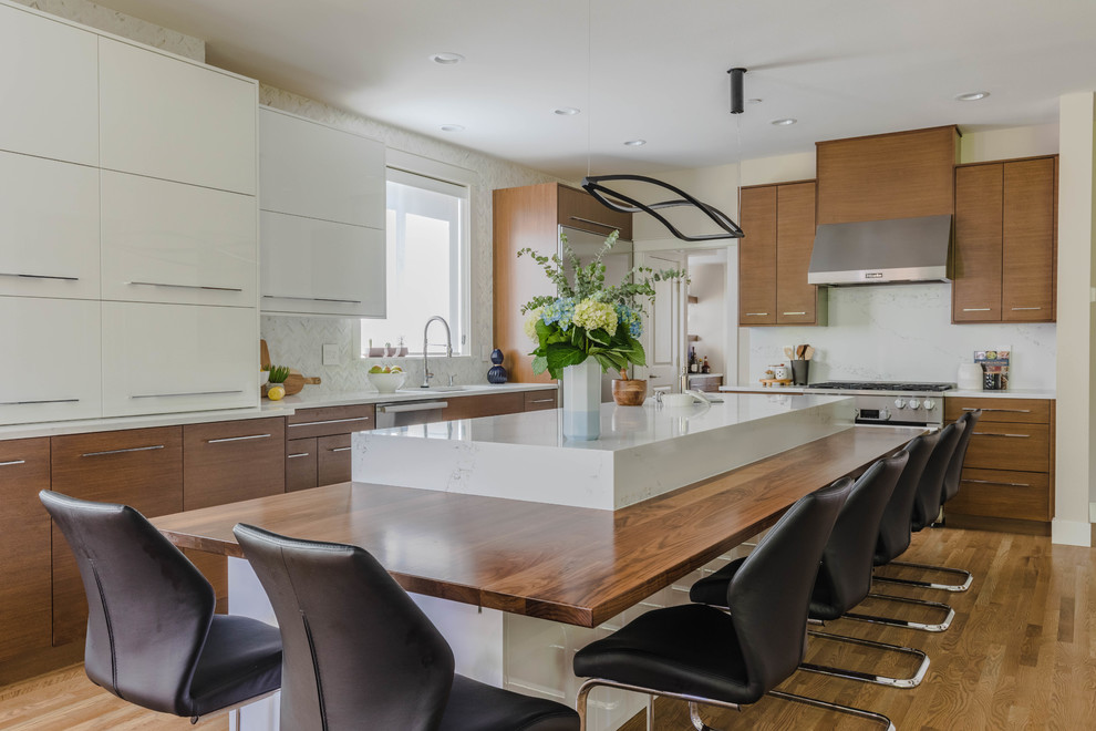 Expansive contemporary l-shaped open plan kitchen in Seattle with an undermount sink, flat-panel cabinets, light wood cabinets, marble benchtops, white splashback, marble splashback, stainless steel appliances, light hardwood floors, with island, brown floor and white benchtop.