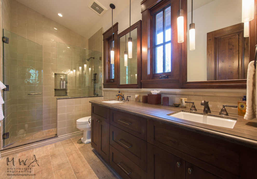 Corner shower - large transitional 3/4 beige tile porcelain tile and brown floor corner shower idea with shaker cabinets, dark wood cabinets, a one-piece toilet, beige walls, an undermount sink, a hinged shower door and brown countertops