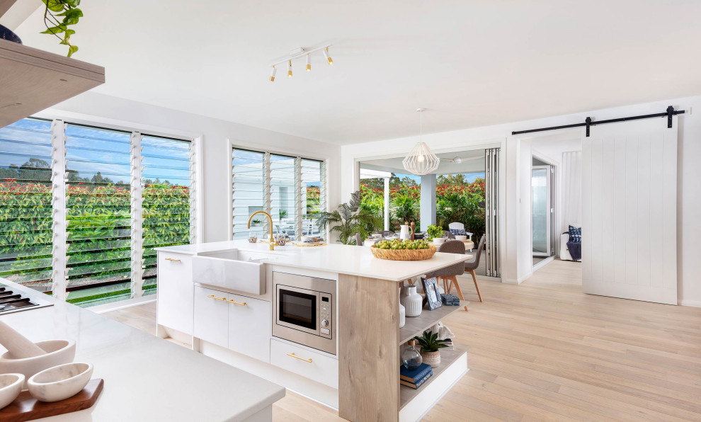 Inspiration for a large beach style l-shaped open plan kitchen in Sydney with an integrated sink, shaker cabinets, white cabinets, quartz benchtops, grey splashback, ceramic splashback, panelled appliances, light hardwood floors, with island, beige floor and white benchtop.