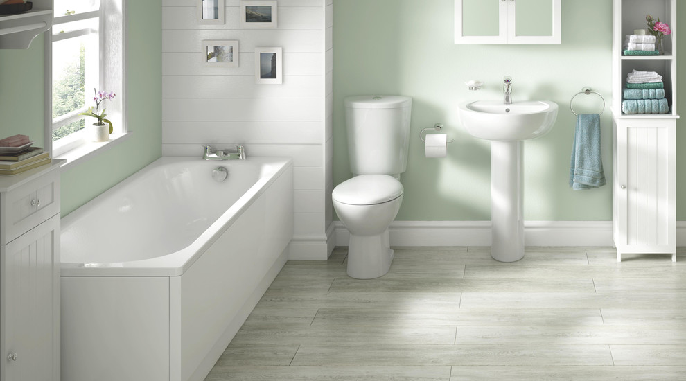 This is an example of a mid-sized contemporary bathroom in Hampshire with a wall-mount sink, white cabinets, a drop-in tub, a one-piece toilet, white tile, green walls and linoleum floors.