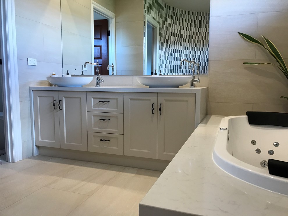 Design ideas for a large modern master bathroom in Sydney with shaker cabinets, beige cabinets, a drop-in tub, a wall-mount toilet, beige tile, porcelain tile, beige walls, porcelain floors, a vessel sink and engineered quartz benchtops.