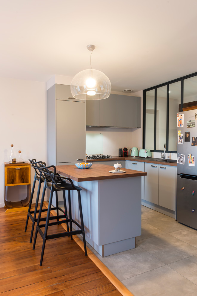 Design ideas for a small contemporary u-shaped open plan kitchen in Grenoble with grey cabinets, wood benchtops, glass sheet splashback, stainless steel appliances, ceramic floors, grey floor, a drop-in sink, flat-panel cabinets, white splashback, a peninsula and brown benchtop.