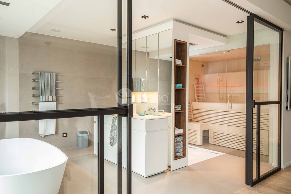 Inspiration for an expansive contemporary bathroom in New York with furniture-like cabinets, white cabinets, a freestanding tub, an open shower, with a sauna, an integrated sink, an open shower, a wall-mount toilet, beige tile, stone tile, beige walls, travertine floors, engineered quartz benchtops, grey floor and white benchtops.